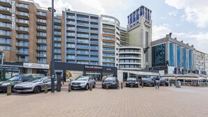 A modern hotel with multiple floors, a prominent entrance, and a parking area with several cars.
