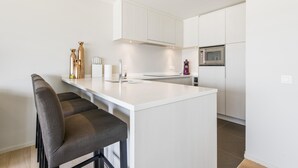 A modern kitchen with white cabinetry, a central island with bar stools, a microwave, and a refrigerator.