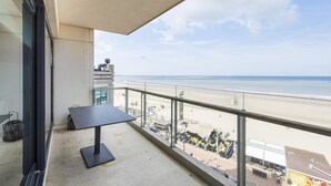 A balcony with a view of the beach, a table, and a trash bin.