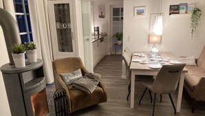 A cozy living room with a fireplace, a dining table set for two, and a comfortable sofa. - Heimathafen Greetsiel (Krummhoern)