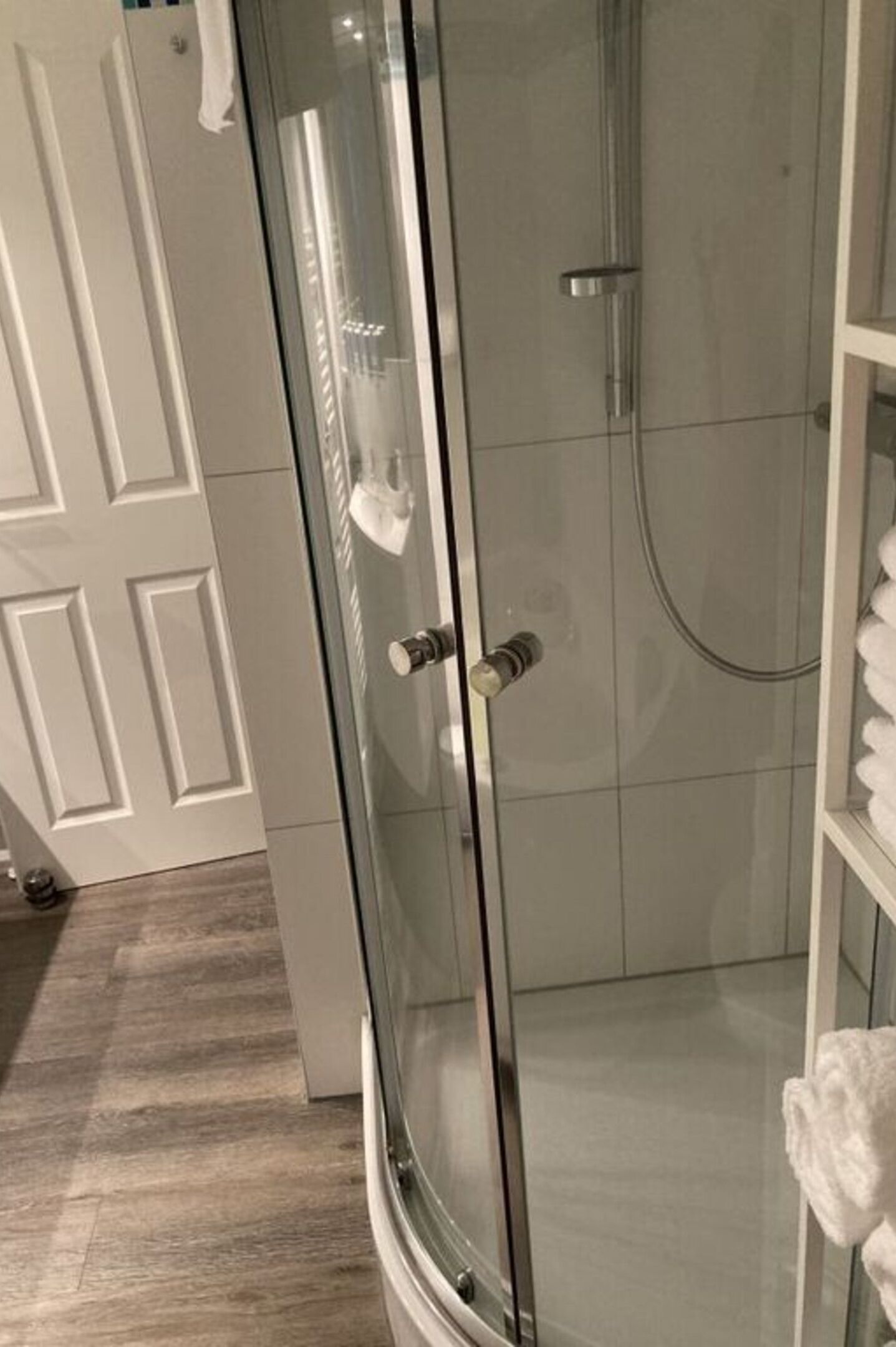 A glass-enclosed shower with a white door, a tiled floor, and a white towel rack.