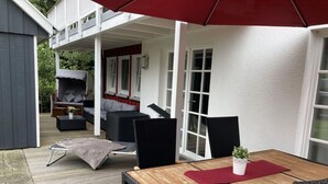 An outdoor patio with a wooden table and chairs, a red umbrella, and a seating area with a sofa and chairs. - Heimathafen Greetsiel (Krummhoern)