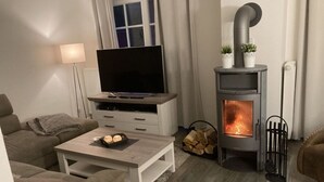 A cozy living room with a fireplace, a television on a wooden stand, and a sofa. - Heimathafen Greetsiel (Krummhoern)