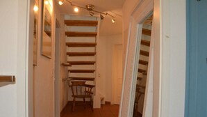 Ein schmaler Flur mit einer Holztreppe und einem Stuhl.