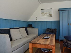 Ett mysigt vardagsrum med en soffa, ett träbord, ett blått skåp och en inramad tavla på väggen.