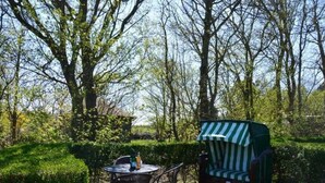 Eine Terrasse mit einem runden Tisch, Stühlen, einem gestreiften Sonnenschirm und einem grünen Stuhl.