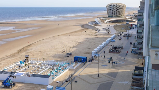 Een strandboulevard met een moderne architecturale constructie, een begraafplaats en helder uitzicht op de zee.