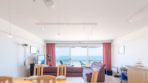 Een moderne eetruimte met een grote tafel, stoelen en uitzicht op de oceaan door grote ramen.