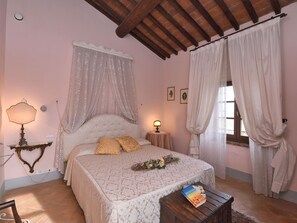 Ein Schlafzimmer mit Bett, Nachttischlampen, einem Nachttisch, einem Fenster mit Vorhängen und einer Wand mit gerahmten Bildern.