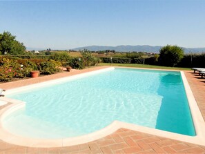 Ein rechteckiger Pool mit geschwungener Kante, umgeben von einer Pflasterterrasse.