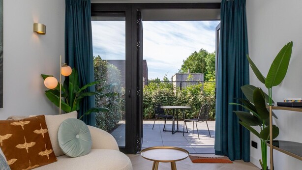 A modern living room with a sofa, a small round table, and a dining area visible through a glass door. - Cozy House in Koudekerke Near the Beach (Koudekerke)