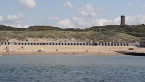 A beach with a row of beach huts, a lighthouse, and a sandy landscape with hills in the background. - Cozy House in Koudekerke Near the Beach (Koudekerke)