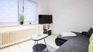 Ett modernt vardagsrum med en soffa, ett litet bord, en tv och ett fönster med persienner.