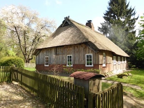 A traditional wooden house with a thatched roof, surrounded by a wooden fence and lush greenery. - Holiday Home Hirtenkate Apartment 1 (Soderstorf)