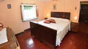 Ein Schlafzimmer mit einem hölzernen Bett, einem Nachttisch mit Lampe, einem Fenster mit Vorhängen und einer Tür.