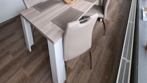 Ein stilvoller Essbereich mit Holztisch, grau gepolsterten Stühlen und einer festen Bank. Eine wandhängende Uhr und Pendelleuchten befinden sich über dem Tisch.