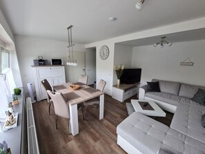 A modern living space with a dining area, a sofa, a TV, and a kitchen. - Holiday Oasis Minten (Cuxhaven)