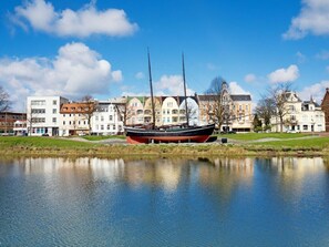 A calm lake with a historic sailing ship docked on the shore, surrounded by traditional European buildings. - Holiday Oasis Minten (Cuxhaven)