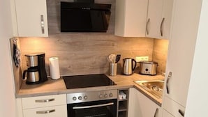 Eine kleine Küche mit weißen Schränken, einer schwarzen Dunstabzugshaube, einem Einbauofen und einer Kaffeemaschine.