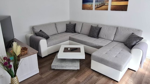 Ein modernes Wohnzimmer mit einem grauen Ecksofa, einem Couchtisch und einem Flachbildfernseher.