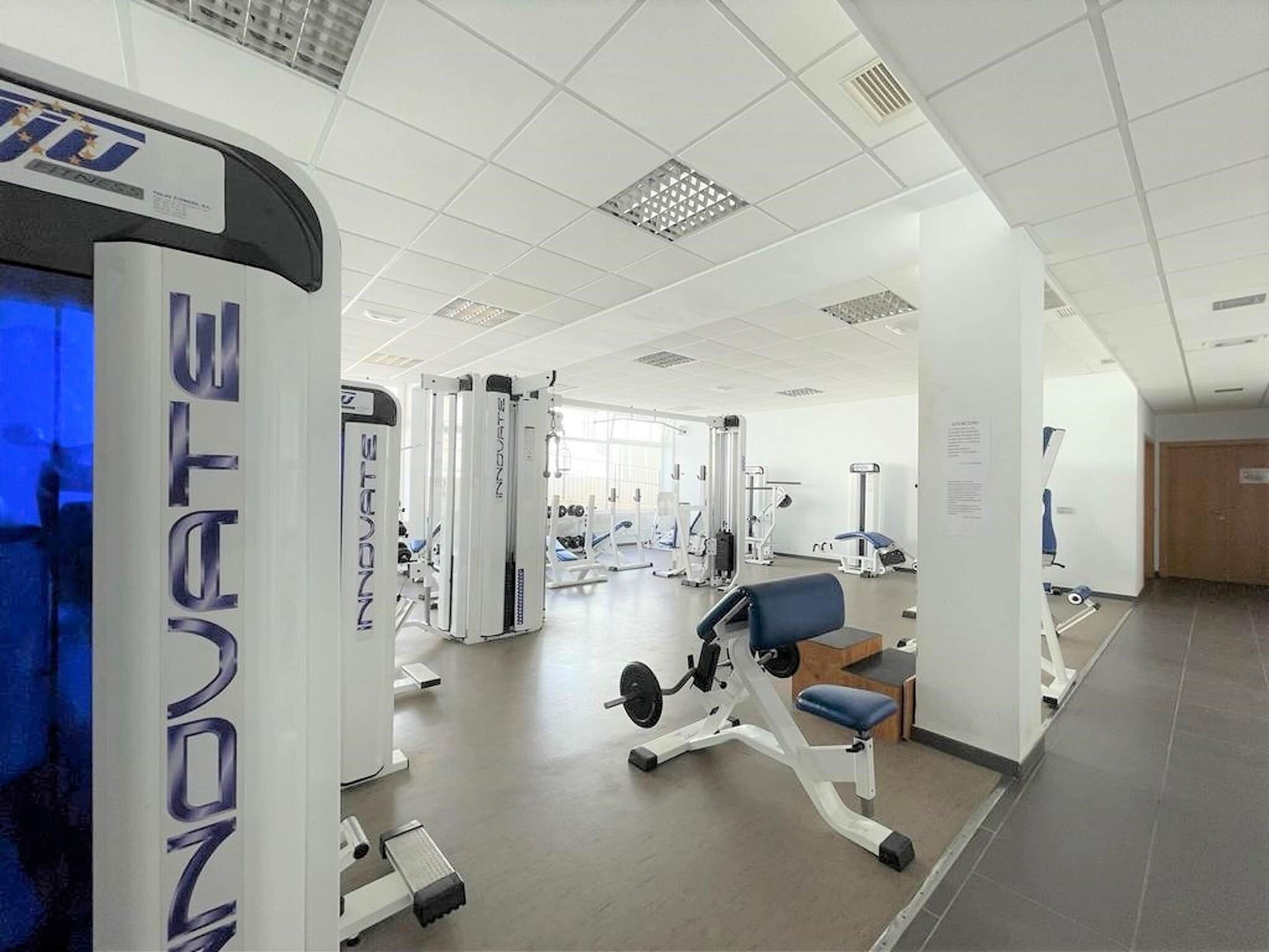 Un gimnasio moderno con diversos equipos de ejercicio, incluyendo cintas de correr y máquinas de pesas.
