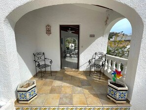 A covered outdoor area with two metal chairs, a tiled floor, and a white wall with a number sign. - Villa With Private Pool in Moraira (Teulada)
