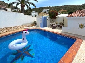 Una piscina con un flotador de unicornio, una palmera y casas al fondo.