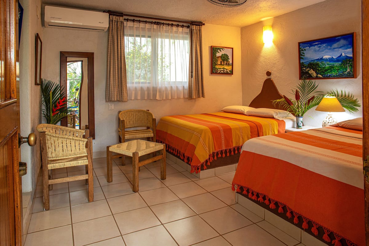 Une chambre d’hôtel avec deux lits, une chaise, une petite table et un tableau au mur.