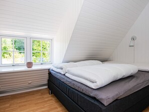 A bedroom with a sloped ceiling, a window with a view of greenery, a bed with white bedding, and a wall-mounted light fixture. - 10 Person Holiday Home in Auning (Auning)