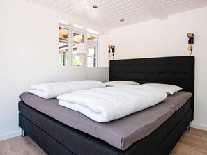 A modern bedroom with a large bed, white bedding, a dark headboard, and a window with a view of the outdoors. - 10 Person Holiday Home in Auning (Auning)