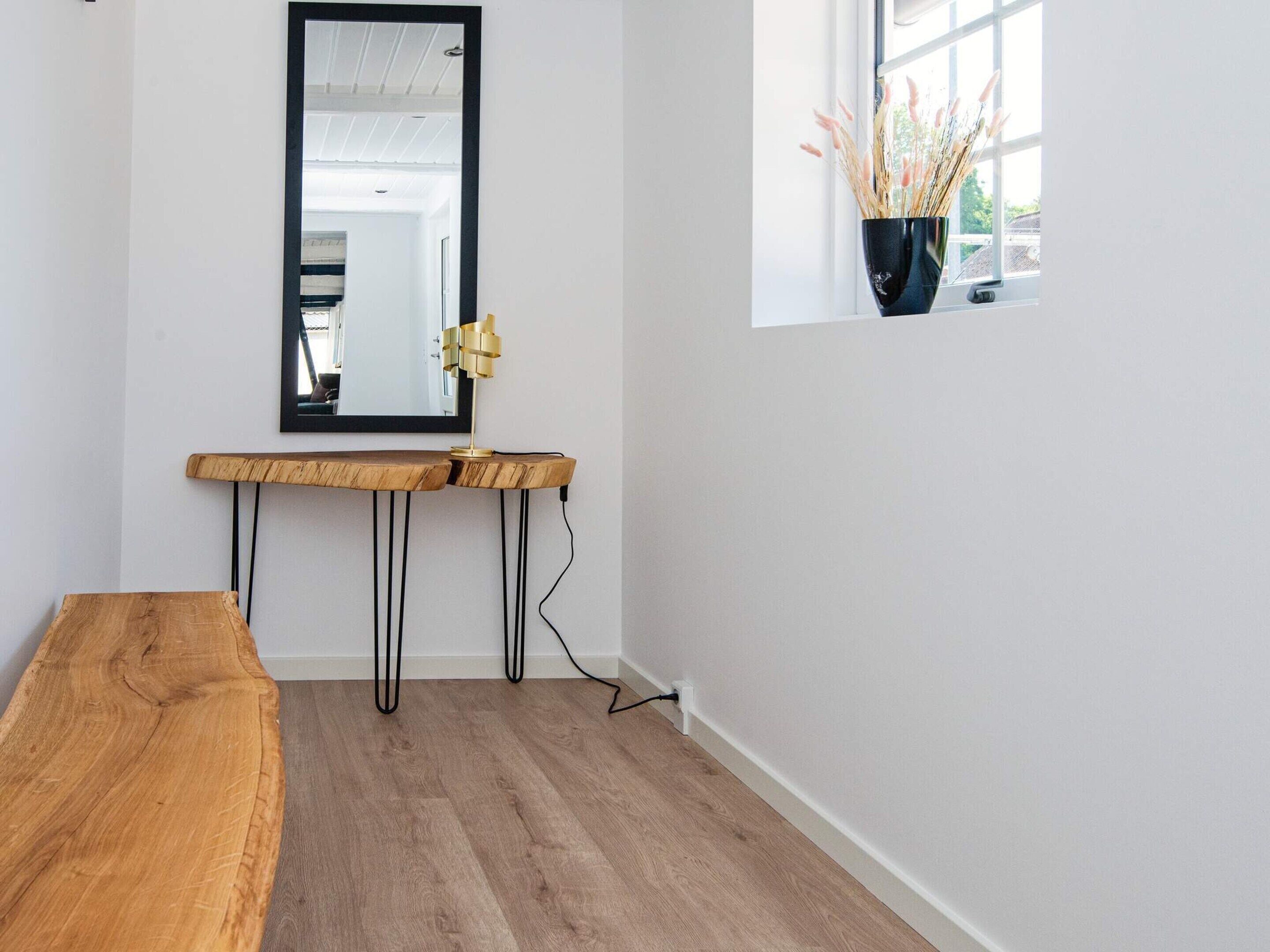 A minimalist room with a wooden bench, a mirror, and a window with a plant.