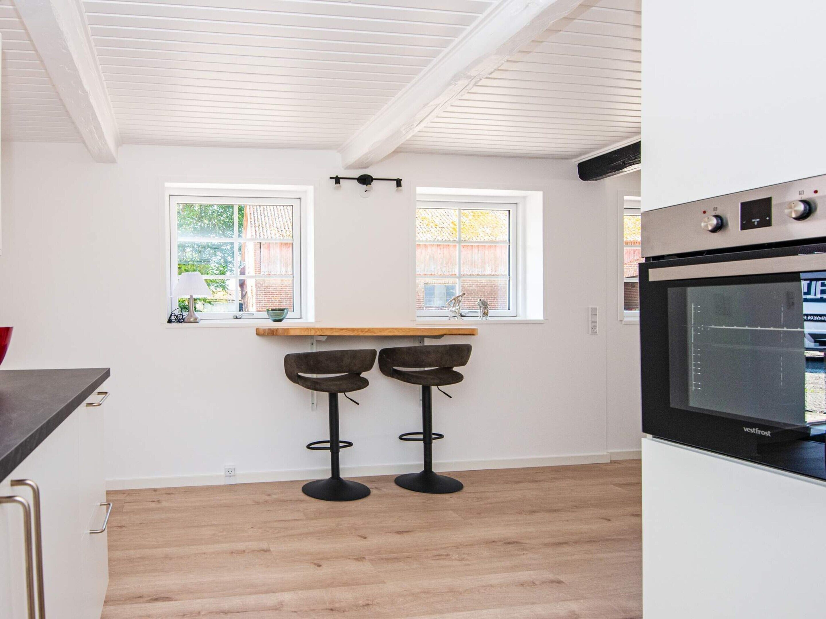 A kitchen with a built-in oven, two windows, and a wooden countertop with stools.