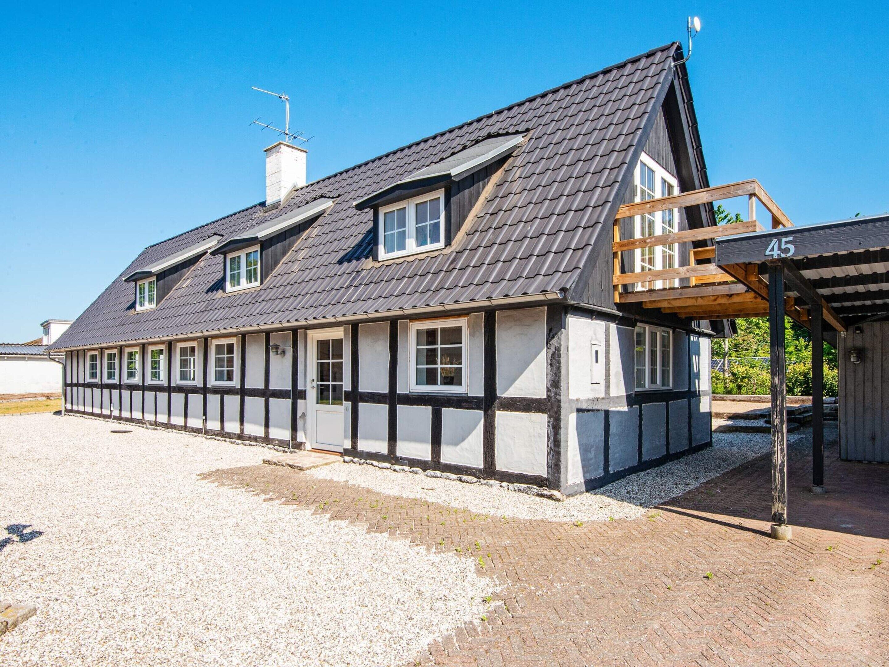 A traditional half-timbered house with a sloped roof, a wooden porch, and a gravel driveway.