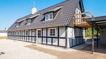 A traditional half-timbered house with a sloped roof, a wooden porch, and a gravel driveway.