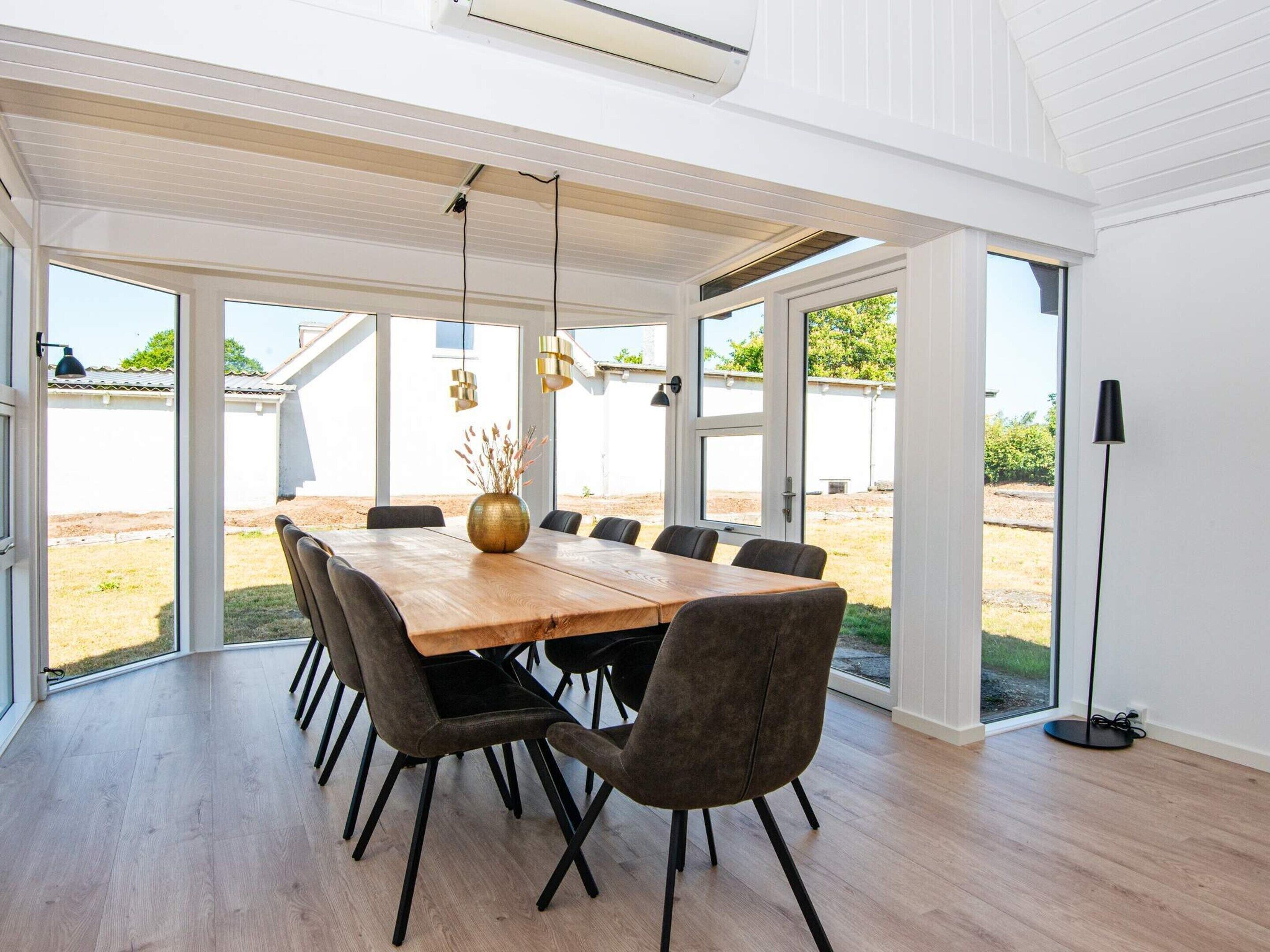 Uma ampla área de jantar com mesa e cadeiras de madeira, janelas grandes e vista para o exterior.