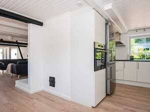A modern kitchen with white cabinetry, a built-in oven, and a window overlooking greenery. - 10 Person Holiday Home in Auning (Auning)