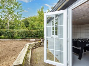 An open door leading to a room with a foosball table, surrounded by a garden with a wooden fence and trees. - 10 Person Holiday Home in Auning (Auning)