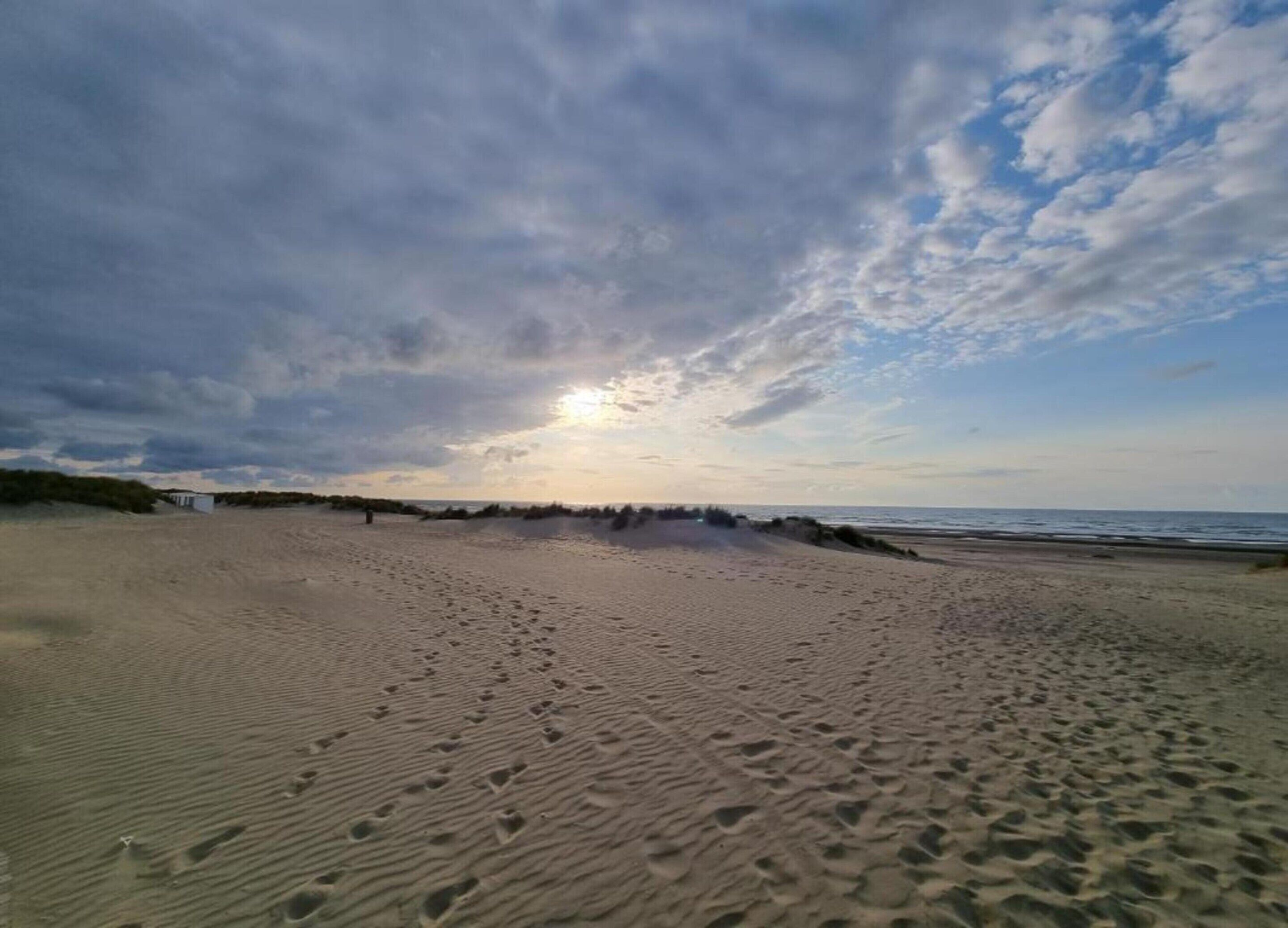 A wide sandy beach with footprints leading towards the ocean, under a partly cloudy sky.