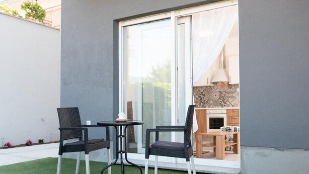 A patio with two chairs and a small table, a sliding glass door leading to a kitchen area, and a grey wall. - Apartments Bella Vista - One Bedroom Apartment With Terrace (Kastav)