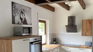 Une cuisine moderne avec des meubles blancs, un four encastré, un micro-ondes et une machine à café. Le plafond est en bois et une fenêtre laisse entrer la lumière naturelle.
