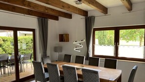 Un coin repas avec une table et des chaises en bois, une lampe et une vue sur la verdure à l’extérieur.
