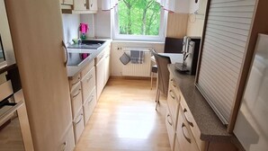 Kompakti keittiö, jossa on puukalusteet, sisäänrakennettu liesi ja ikkuna, josta avautuu näkymä vehreään maisemaan.