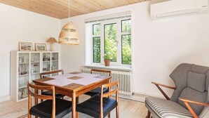En matplats med ett träbord och stolar, en hänglampa i rotting, ett element och ett fönster med utsikt över grönskan.