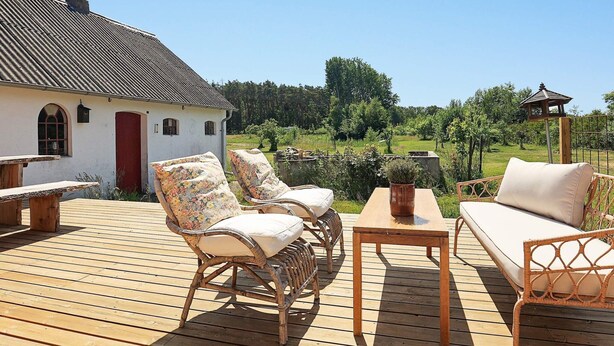 En träveranda med möbler av rotting, ett bord och en röd dörr till en vit byggnad.