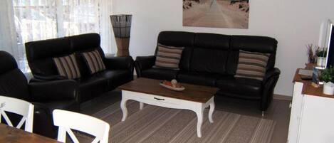 A living room with a black sofa set, a wooden coffee table, a white side table, and a painting of a beach scene.