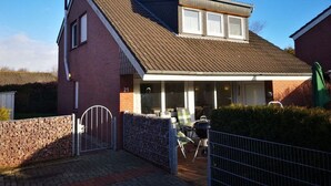 A two-story house with a covered porch, a brick exterior, and a metal gate. - \"seagull Street\" 21 Merchant (Wangerland)