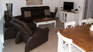 A living room with a sofa, coffee table, TV, and dining area. - \"seagull Street\" 21 Merchant (Wangerland)