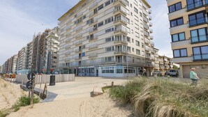 A multi-story residential building with balconies, a sandy ground level, and a pedestrian walkway. - Bright Apartment With Frontal sea View (Middelkerke)