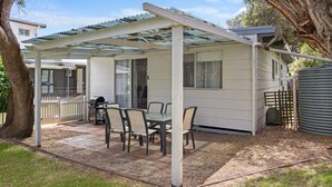 A covered patio with a table and chairs, a grill, and a fenced area. - Prom Coast - Duneside (Sandy Point)