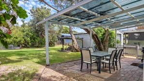 A covered patio with a table and chairs, surrounded by a grassy yard and trees.